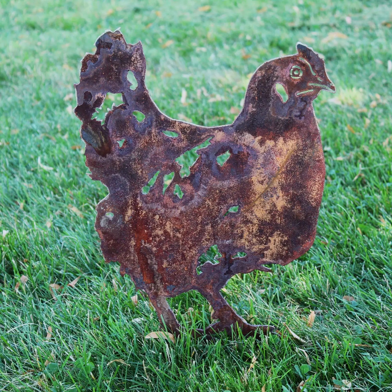 Rustic chicken silhouette made from weathering Corten steel, featuring a patina finish, nestled in green grass.