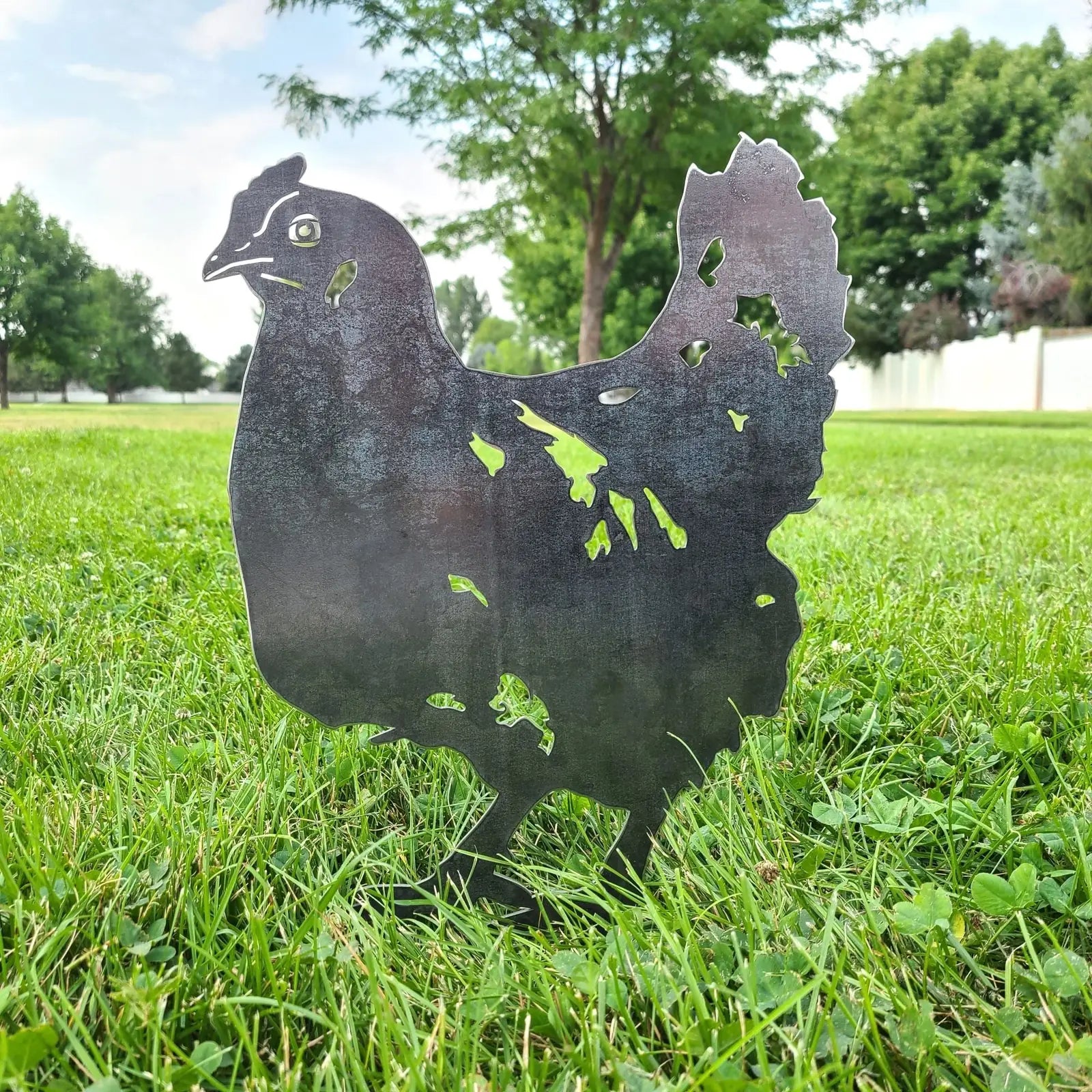 Corten steel chicken silhouette standing in green grass, adding rustic charm to outdoor garden decor.
