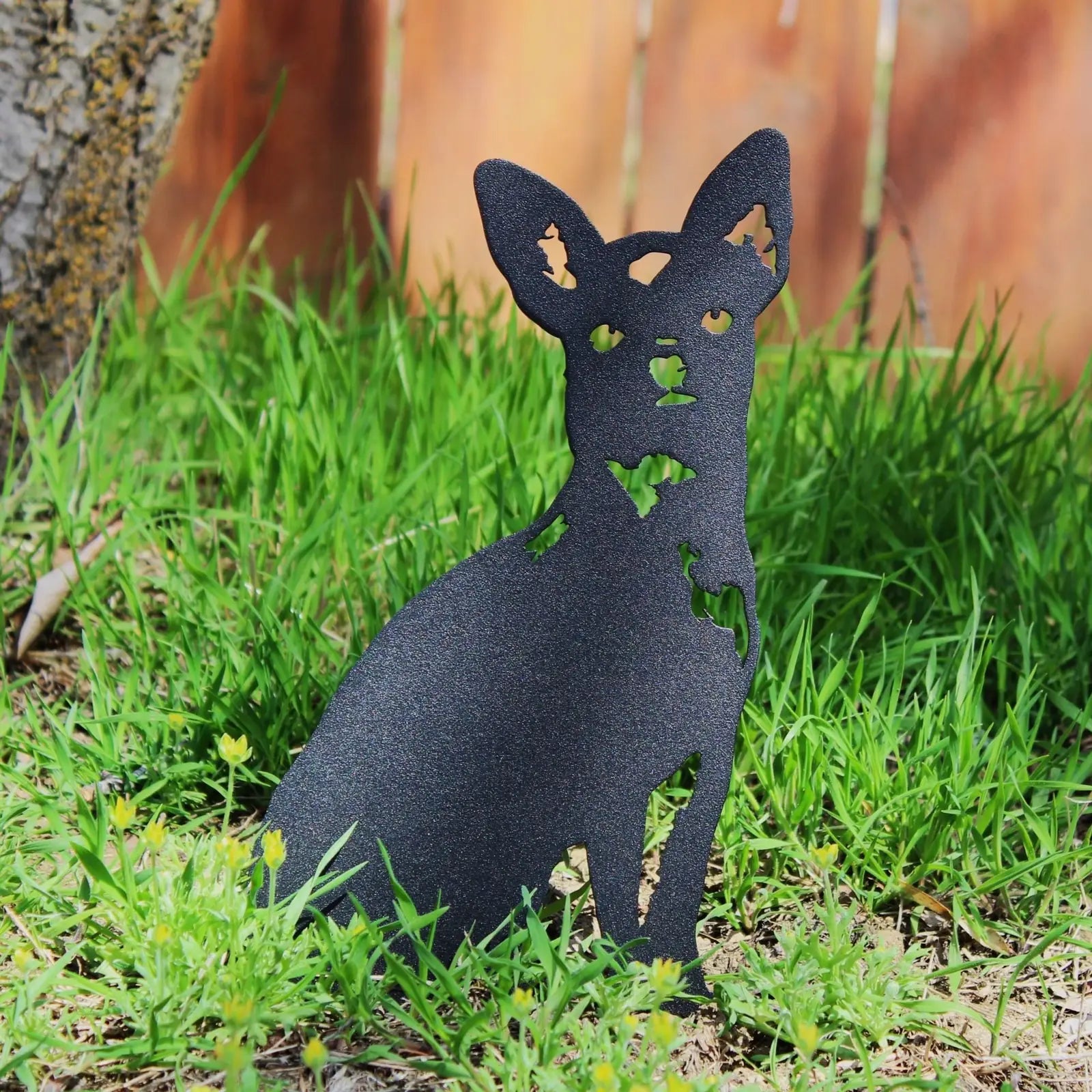 Black metal silhouette of a Chihuahua dog, sitting in vibrant green grass, ideal for outdoor decor.