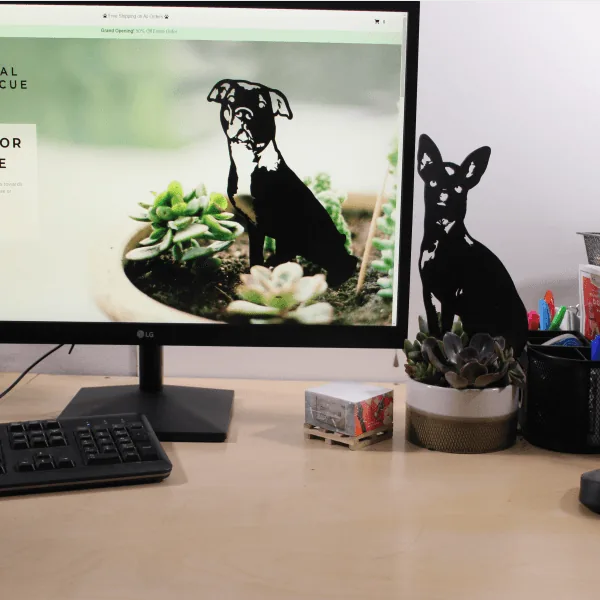 Black metal silhouette of a dog, displayed on a desk next to plants and a computer monitor.