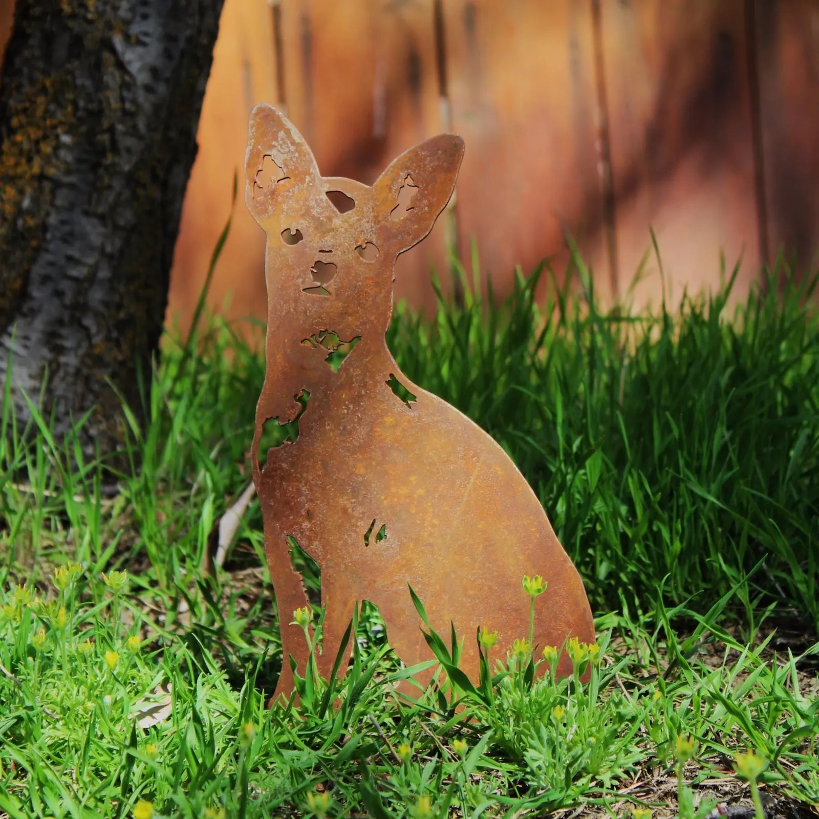 Rusty metal silhouette of a Chihuahua sitting among green grass, ideal for outdoor garden decor.
