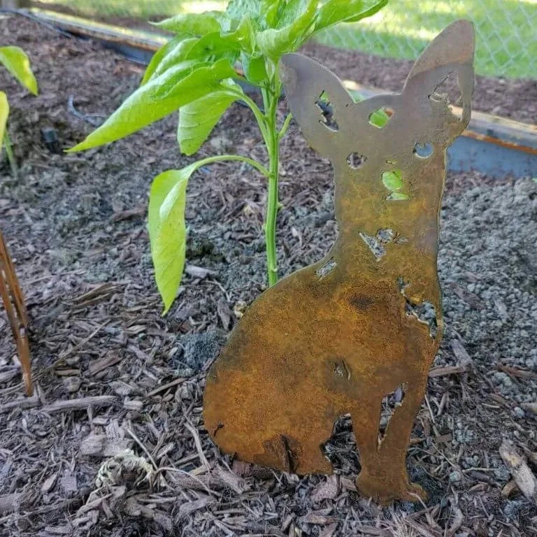 Corten steel silhouette of a Chihuahua nestled among plants, showcasing a rustic patina in garden decor.