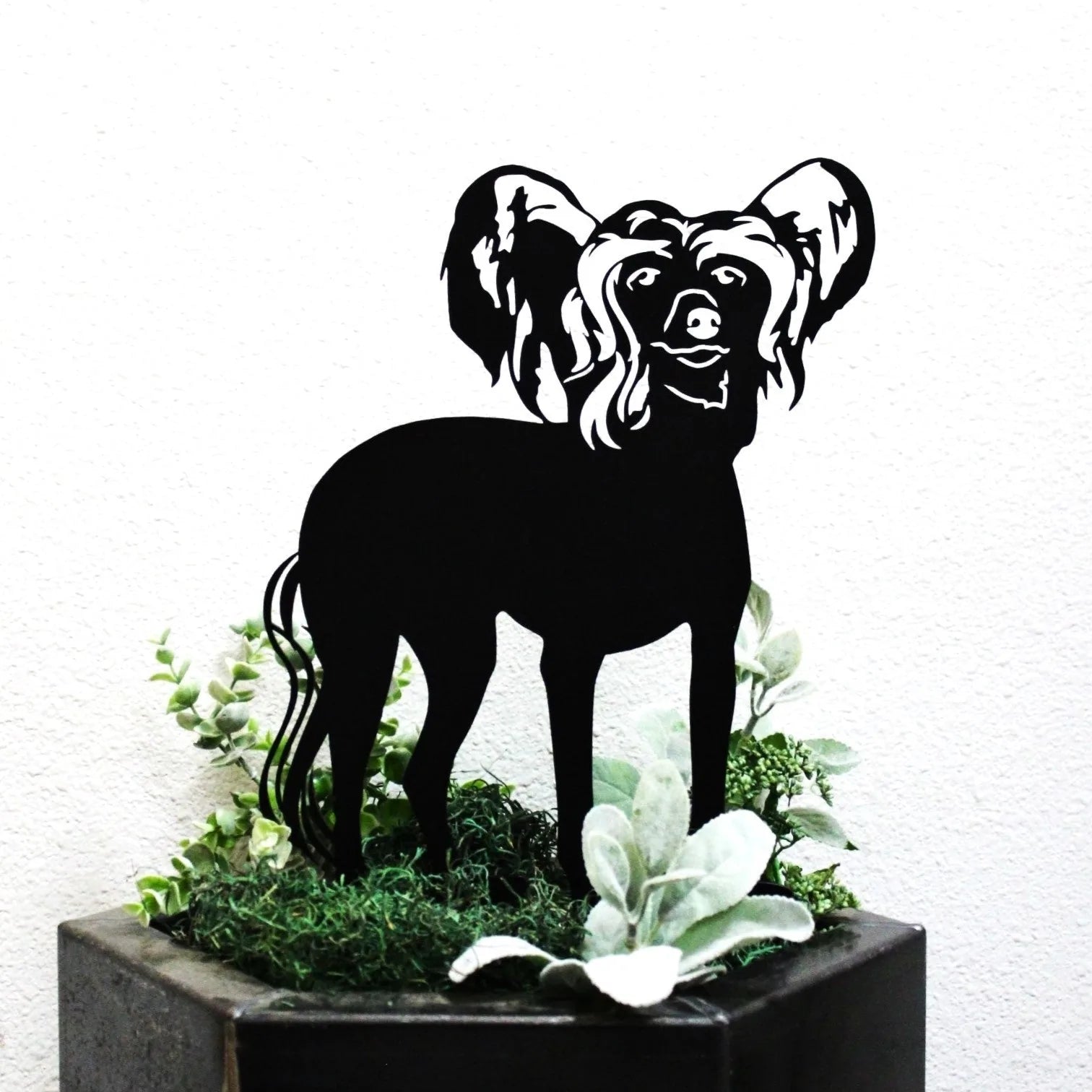Black metal silhouette of a Chinese Crested dog, displayed in greenery, ideal for outdoor decor.