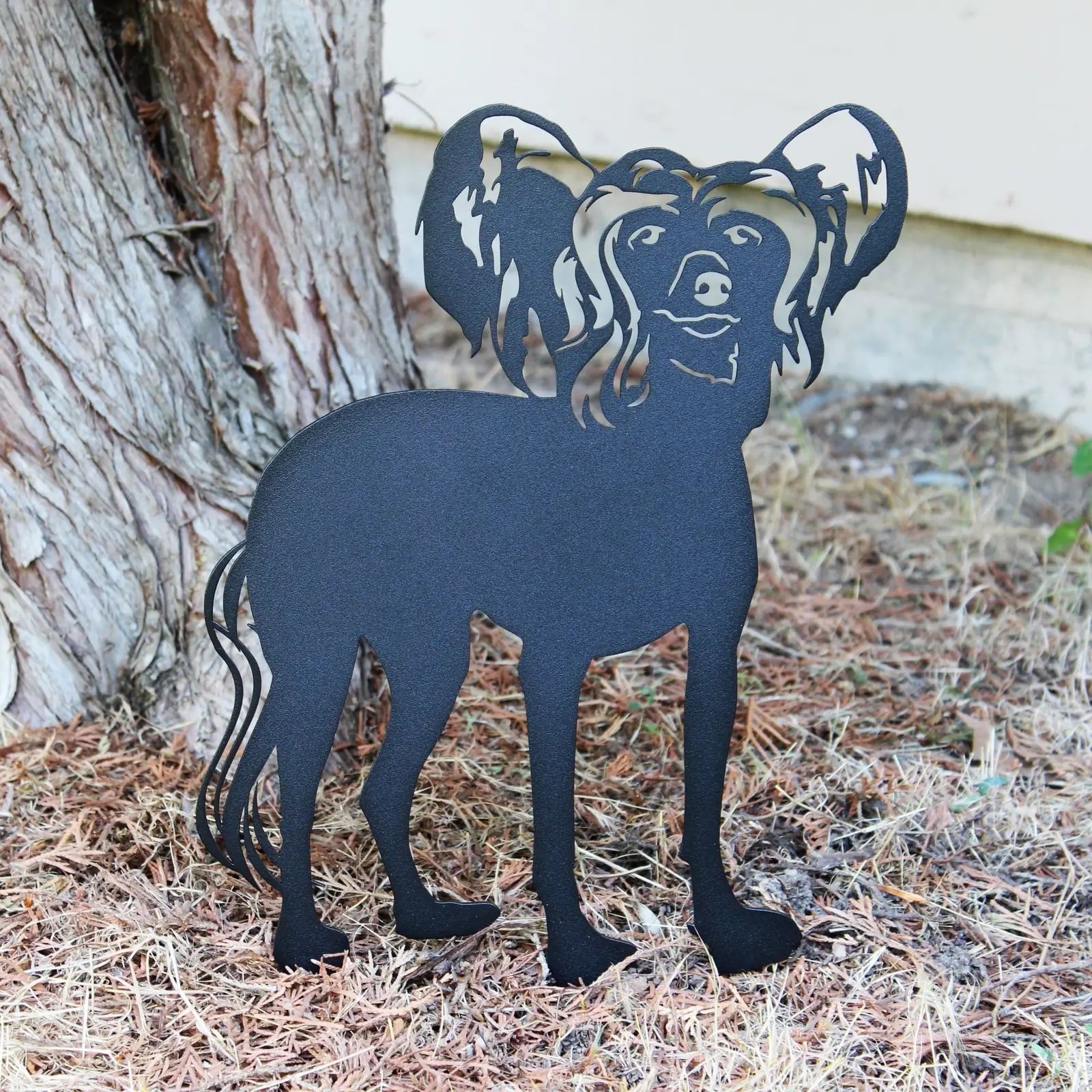 Black metal silhouette of a Chinese Crested dog, displayed outdoors among pine needles. Ideal for garden decor.