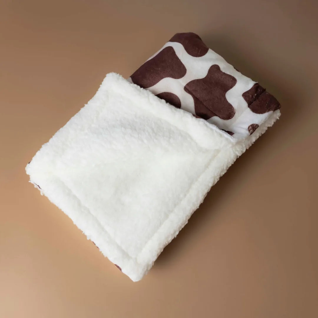 Chocolate Cow Dog Blanket featuring a soft cream sherpa side and a brown and white cow print pattern.