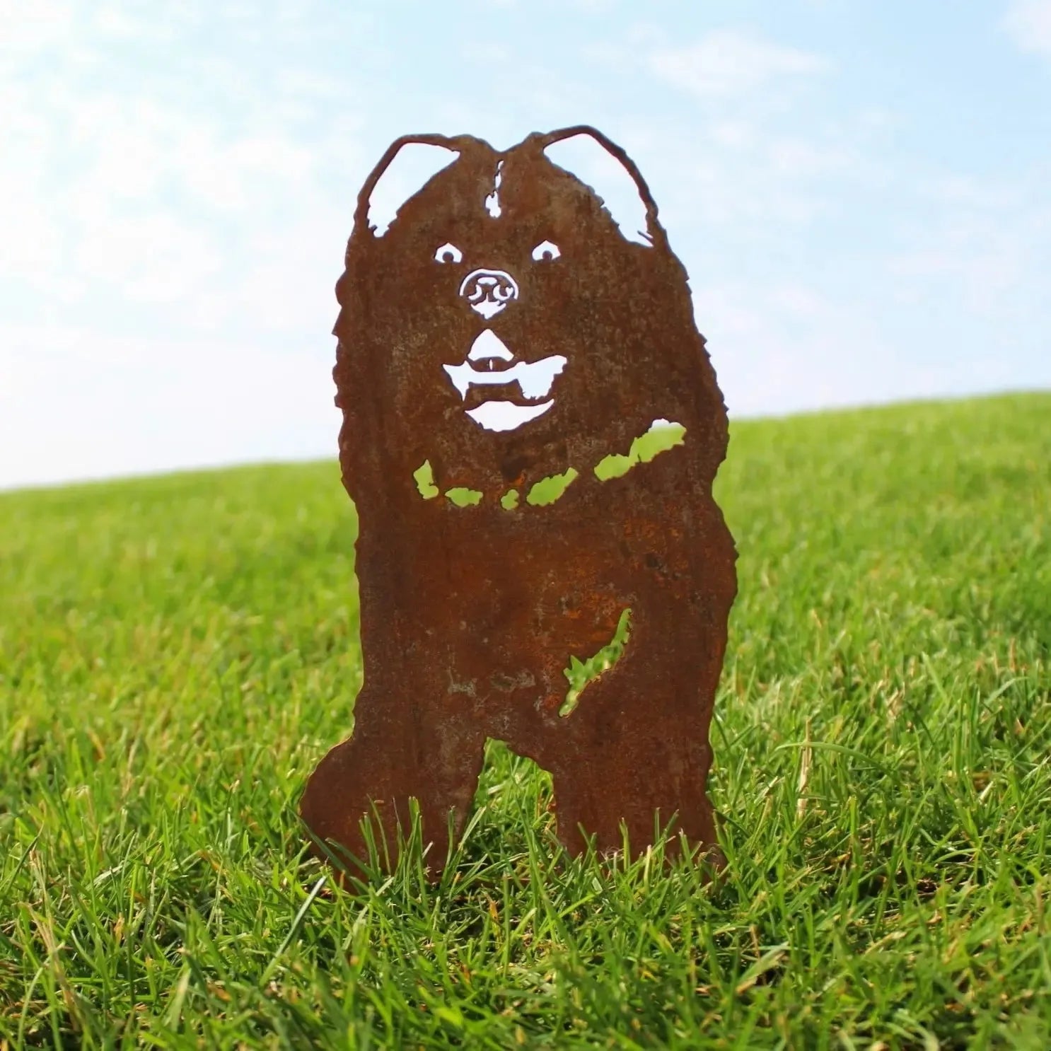 Rusty metal silhouette of a Chow Chow dog, standing on green grass with a clear blue sky in the background.