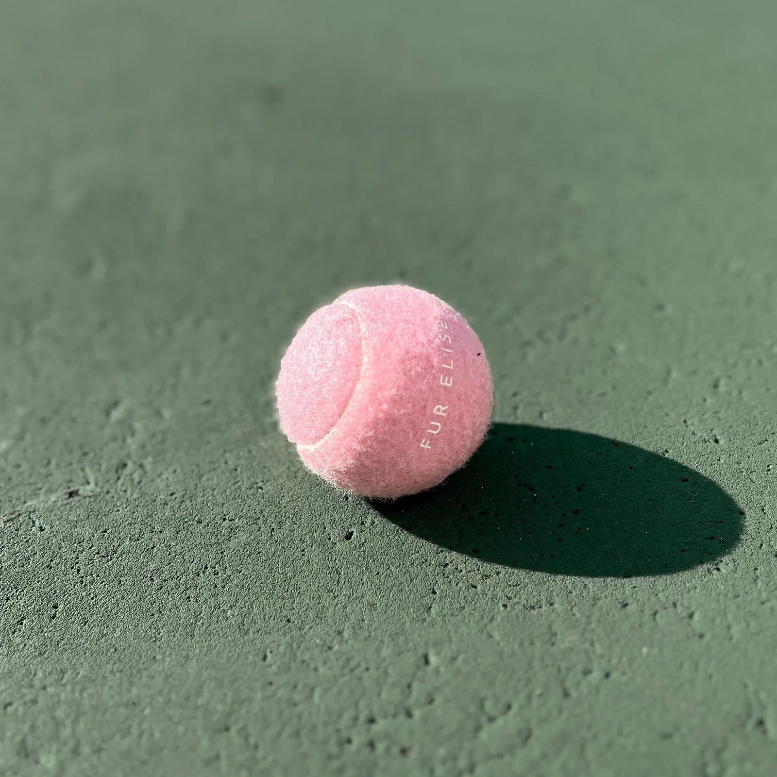 Classic rose tennis ball for dogs, featuring a soft felt exterior and durable rubber core, resting on a green surface.