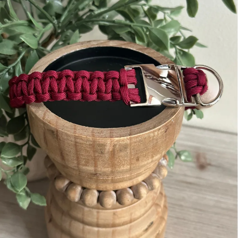 Handmade maroon cobra braid dog collar with a shiny silver buckle resting on a rustic wooden pedestal.