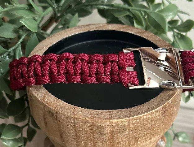 Handmade maroon cobra braid dog collar with a side release buckle, resting on a wooden bowl with greenery.