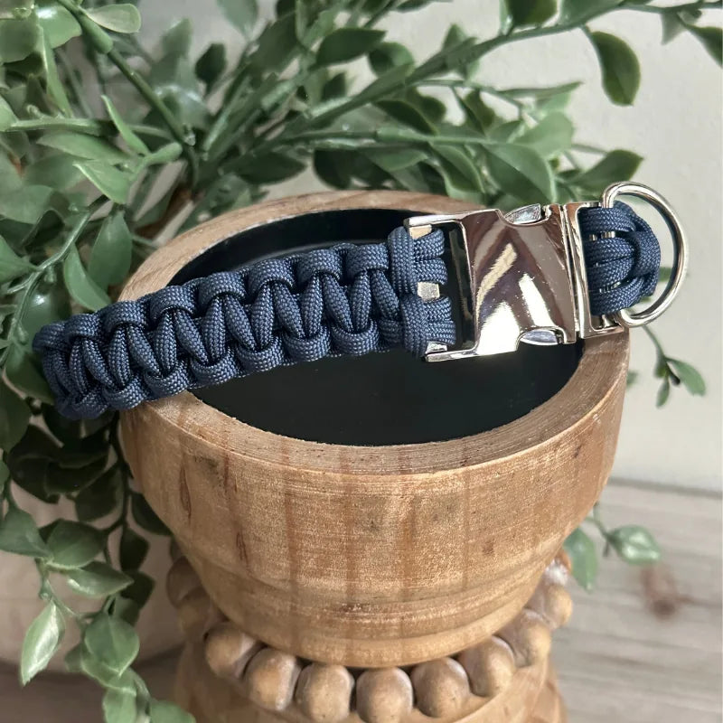 Navy blue handmade braided dog collar featuring a silver buckle and sturdy D-ring, displayed in a wooden bowl.