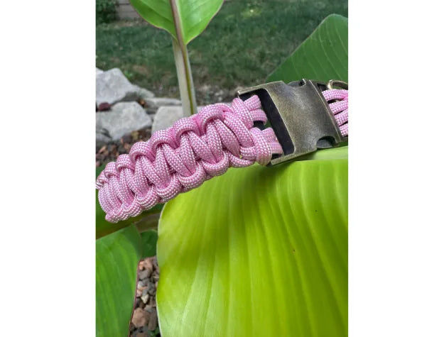 Handmade pink and white braided dog collar resting on a large green leaf, featuring a sturdy side release buckle.