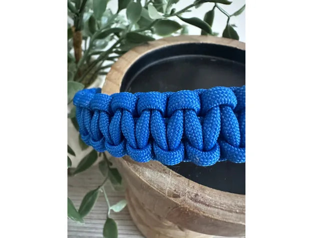 Handmade Cobra Braid dog collar in vibrant blue nylon paracord, displayed beside a wooden bowl and greenery.