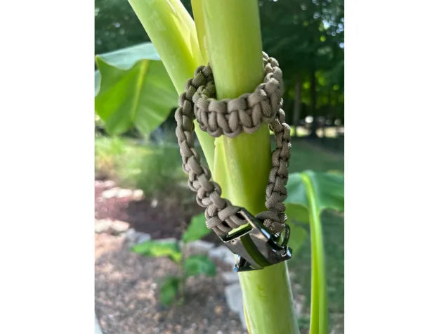 Tan handmade braided dog collar made from premium nylon paracord, displayed on a green plant stem.