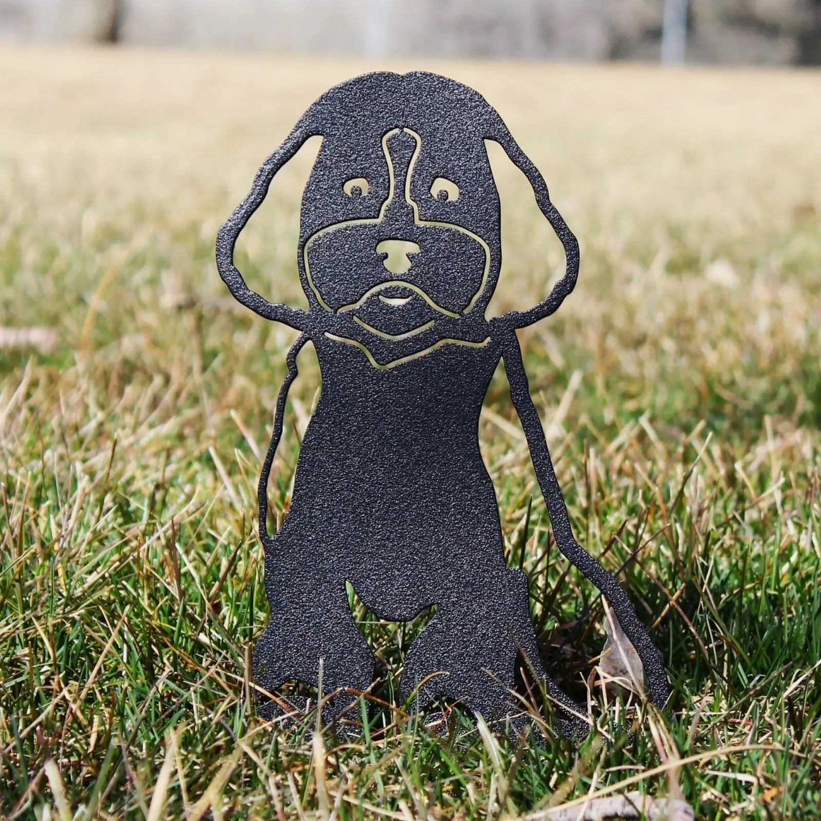Cockapoo metal silhouette in matte black rests on grass, showcasing detailed cutouts and sturdy design for garden decor.
