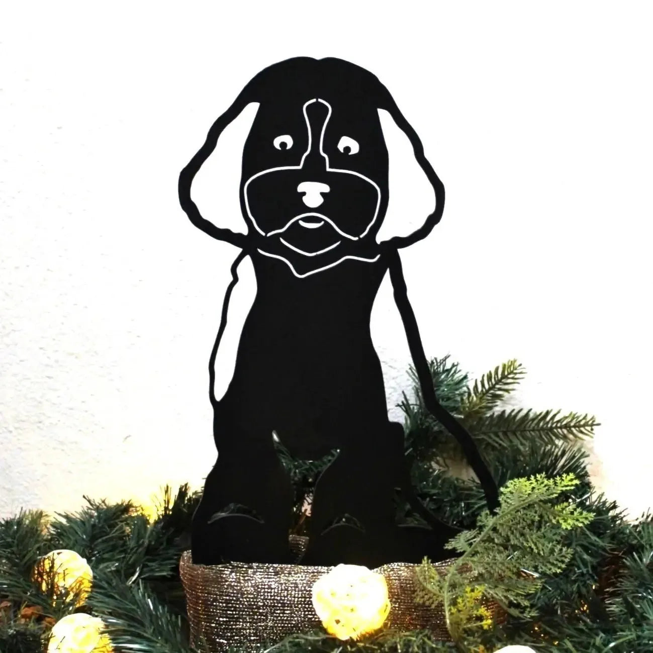 Black metal silhouette of a Cockapoo dog, featuring expressive details, surrounded by greenery and soft lights.