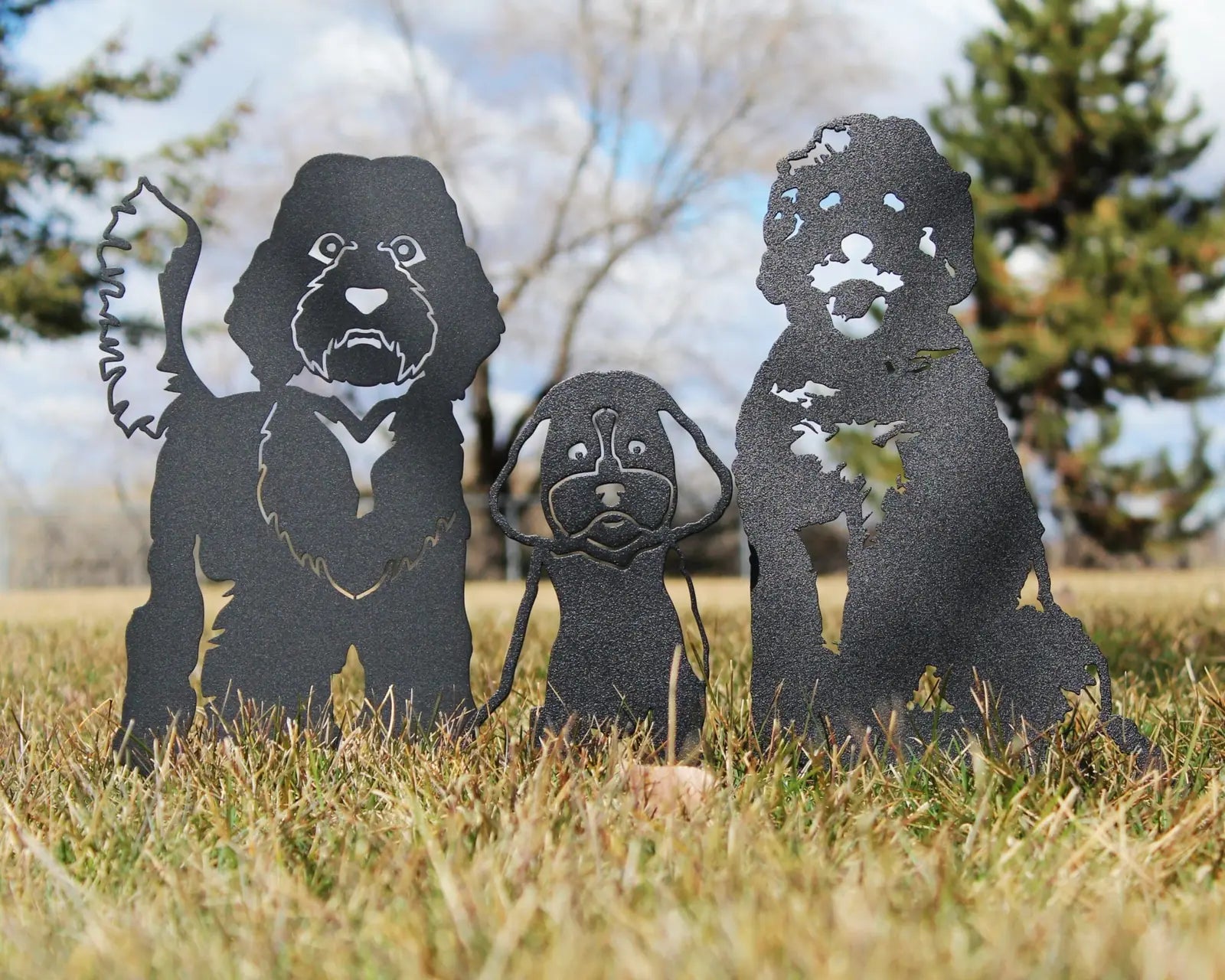 Black metal silhouettes of three dogs in a grassy yard, showcasing Cockapoos in varying poses and sizes.