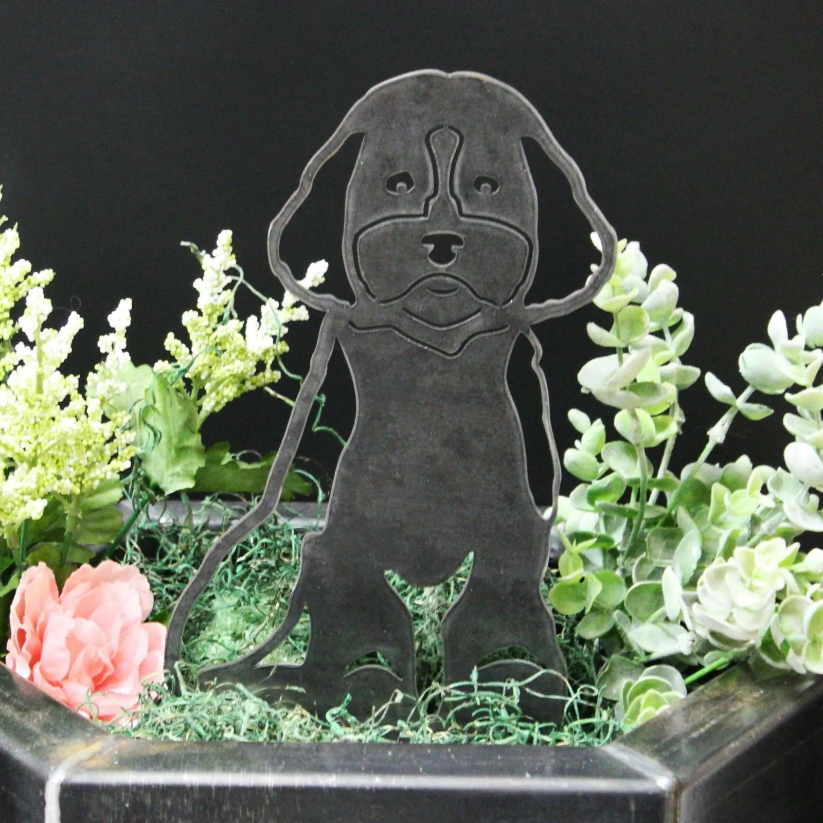 Cockapoo metal silhouette in matte black, featuring a detailed design, surrounded by greenery and flowers in a garden sett...