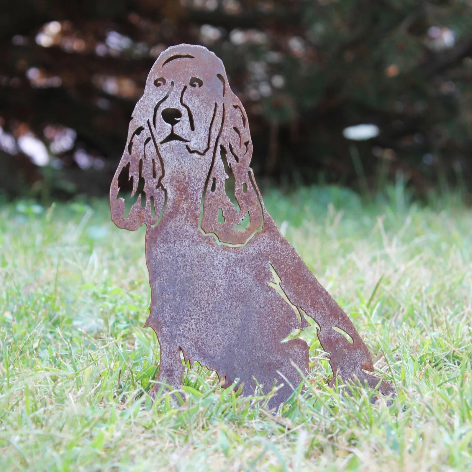 Rusty Cocker Spaniel silhouette made from Corten steel, set on green grass in an outdoor space.