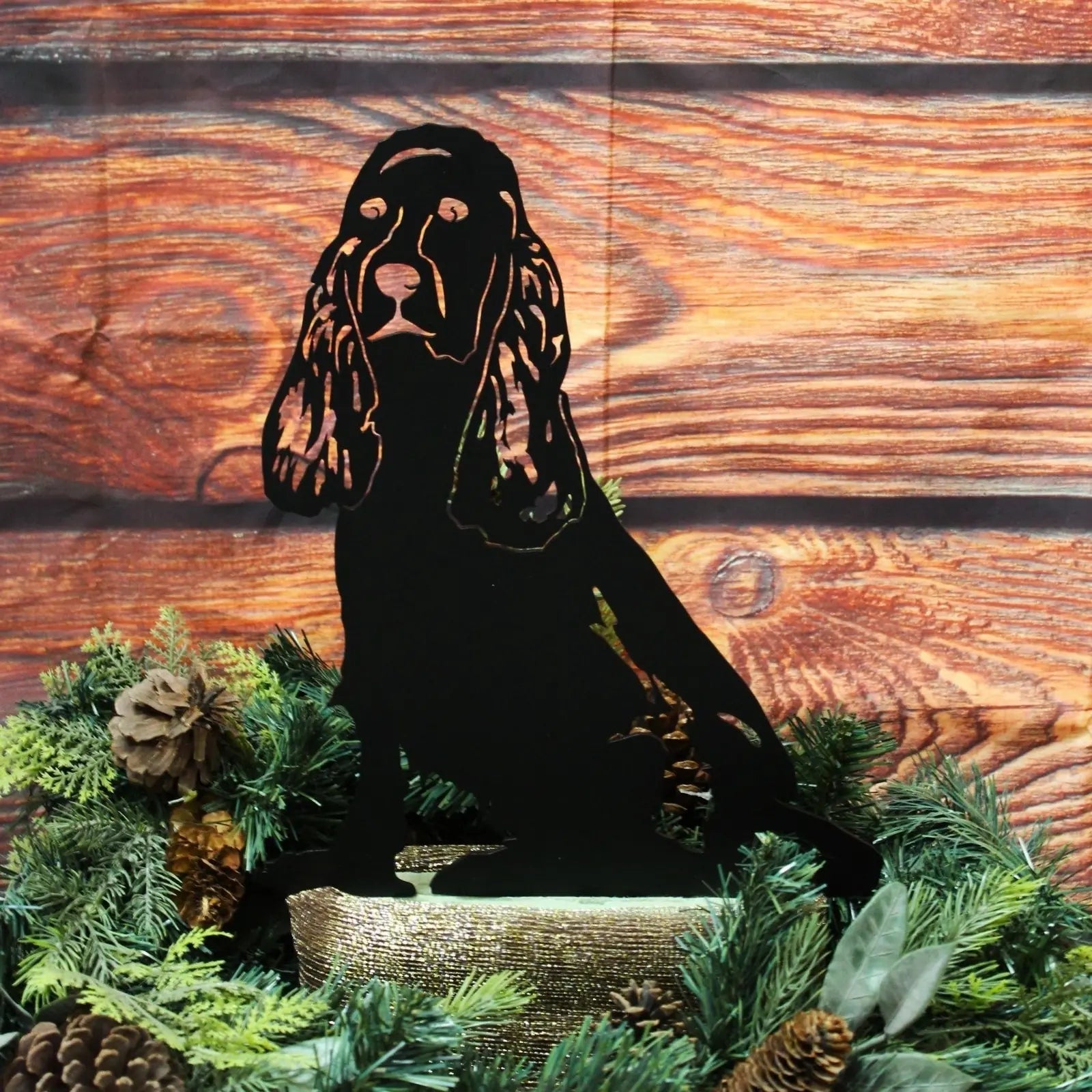 Black Cocker Spaniel metal silhouette art displayed among greenery and pinecones on a wooden background.