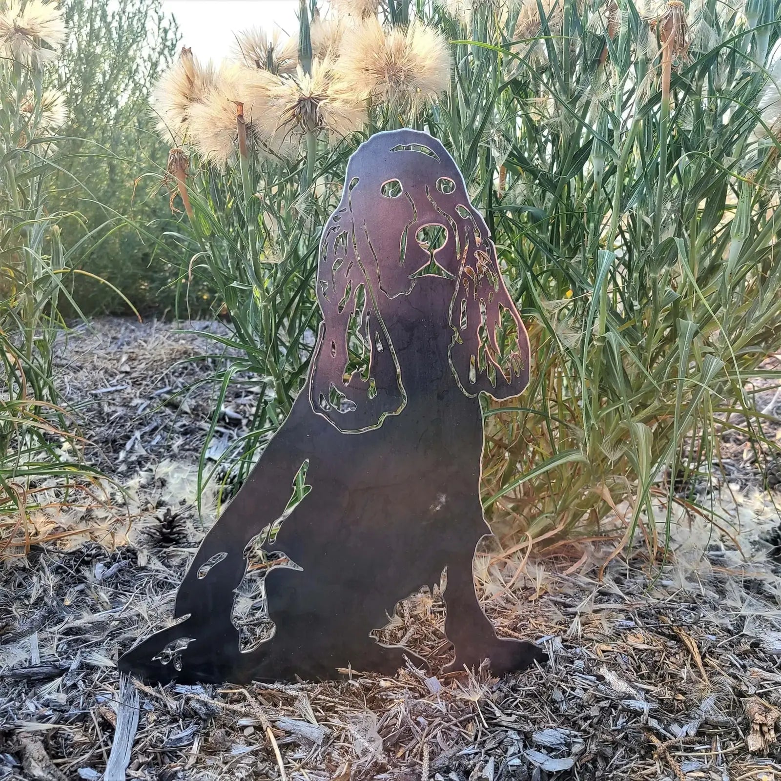 Cocker Spaniel metal silhouette in matte black, set against background of tall grass and wildflowers, showcasing outdoor d...