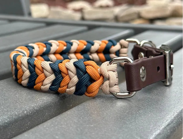 Hand-braided dog collar in mustard, navy, and light tan with a brown adjustable strap and nickel-plated buckle.