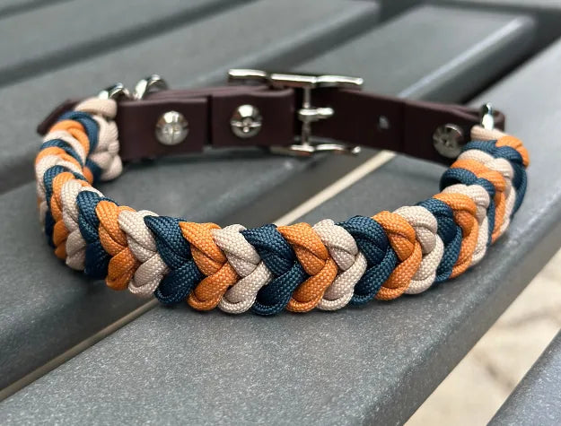 Hand-braided dog collar in mustard, navy, and light tan with a dark brown adjustable strap and nickel-plated buckle.