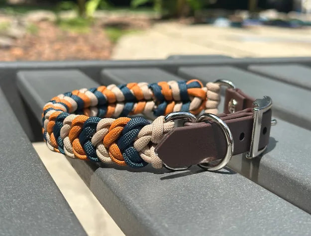 Hand-braided dog collar in mustard, navy, and light tan with a brown adjustable strap and metal D-ring for leash attachment.