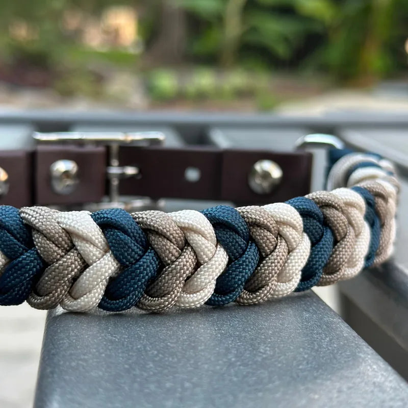 Hand-braided dog collar in navy, tan, and cream nylon paracord with a dark brown adjustable strap and nickel plated buckle.
