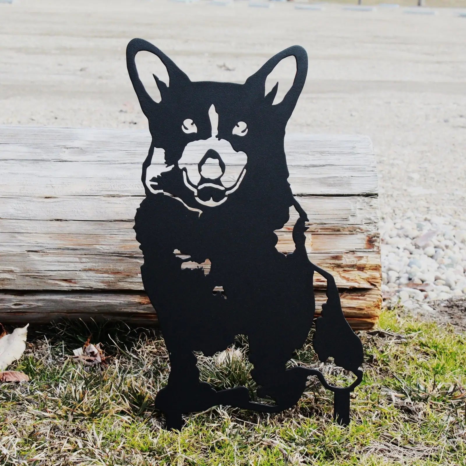 Corgi metal silhouette in matte black, standing on grass near a log, ideal for outdoor garden decor.