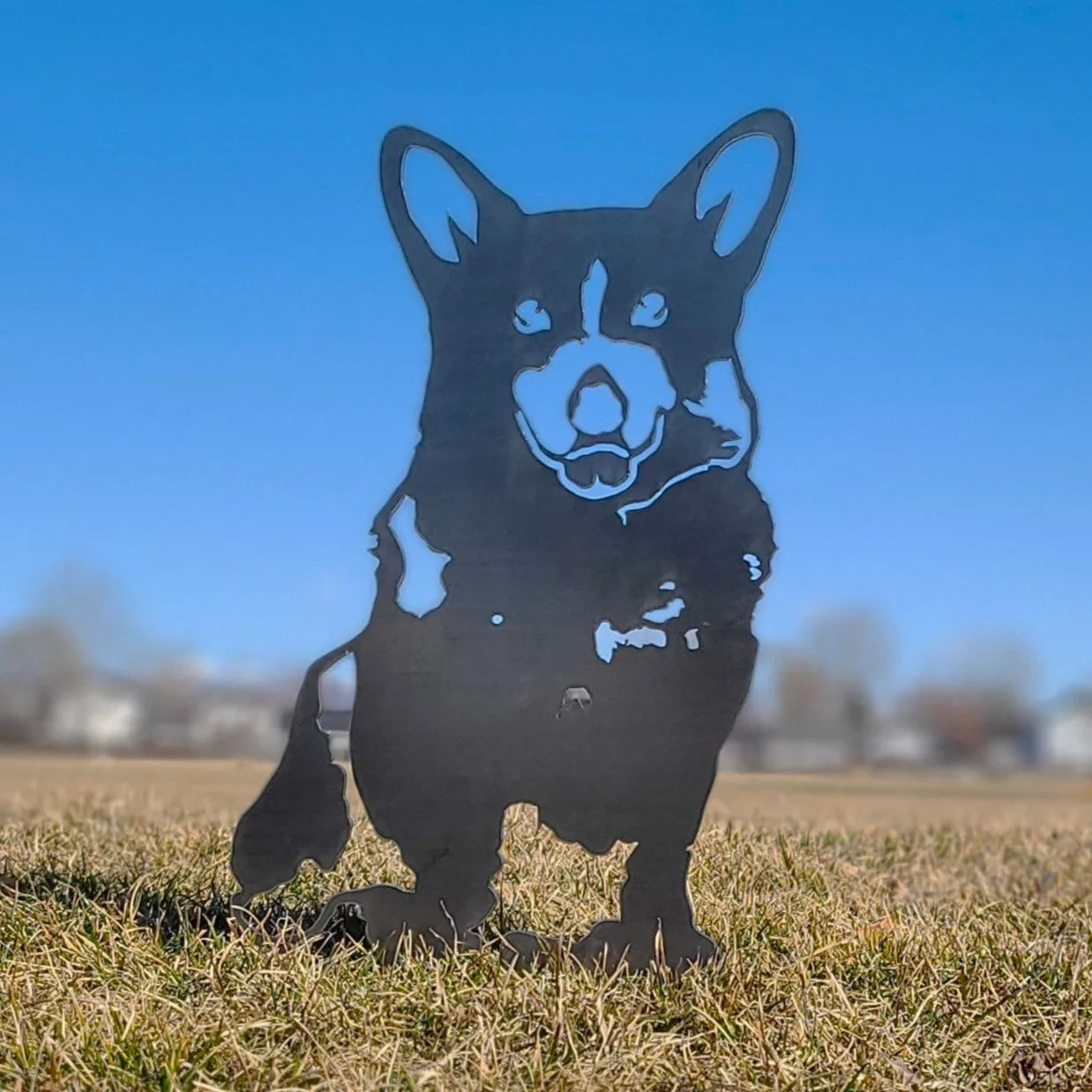 Corgi metal silhouette in matte black stands in grass, capturing the breed's playful character against a blue sky.