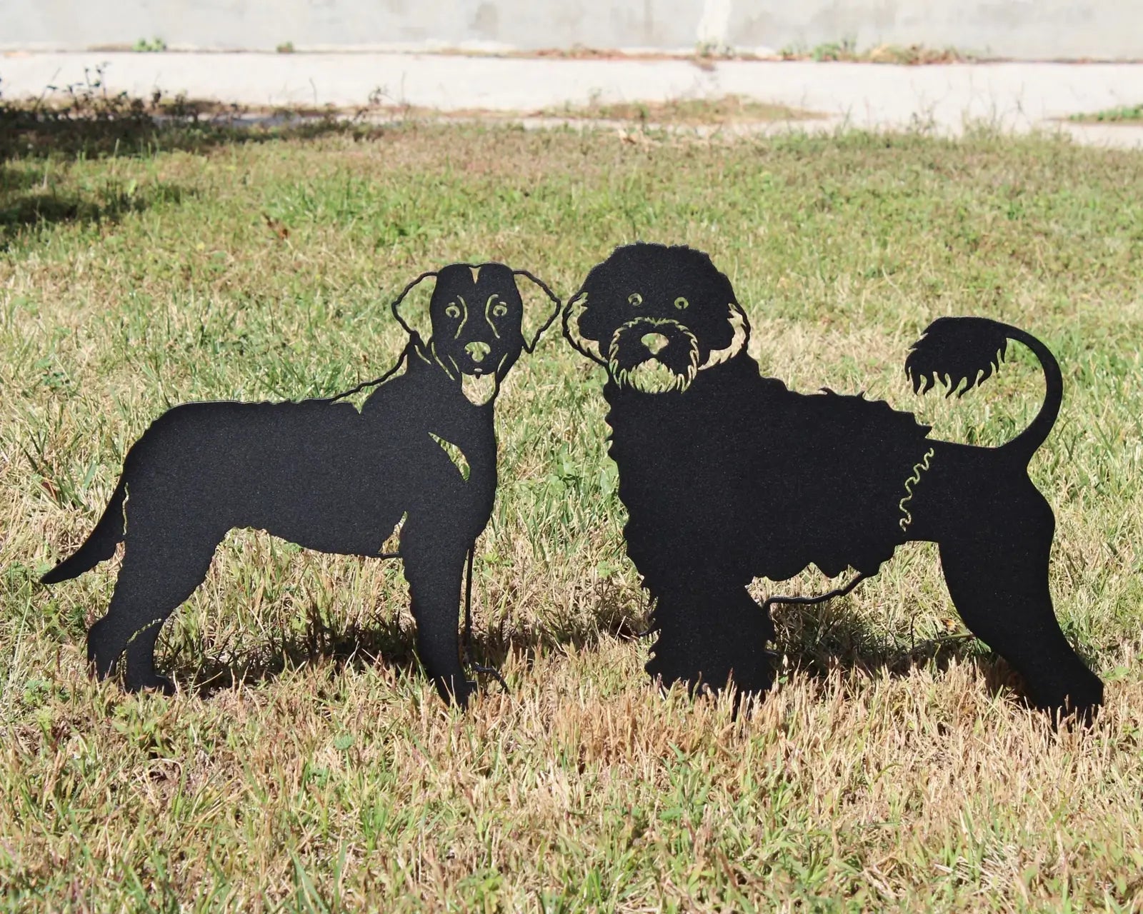 Curly Coated Retriever and Labrador silhouettes in black metal, set against a grassy outdoor backdrop.
