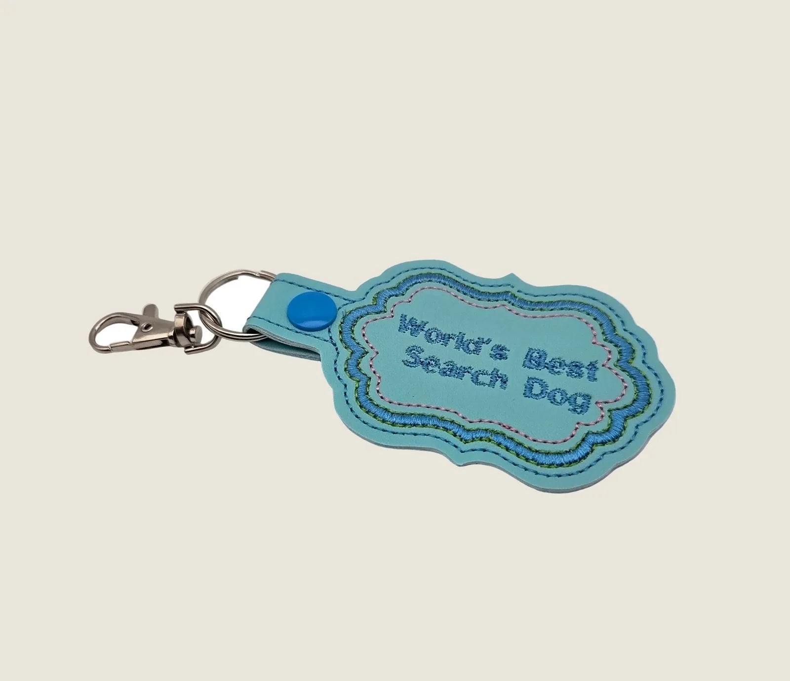 Custom embroidered keychain in blue faux-leather, featuring "World's Best Search Dog" with colorful stitching.