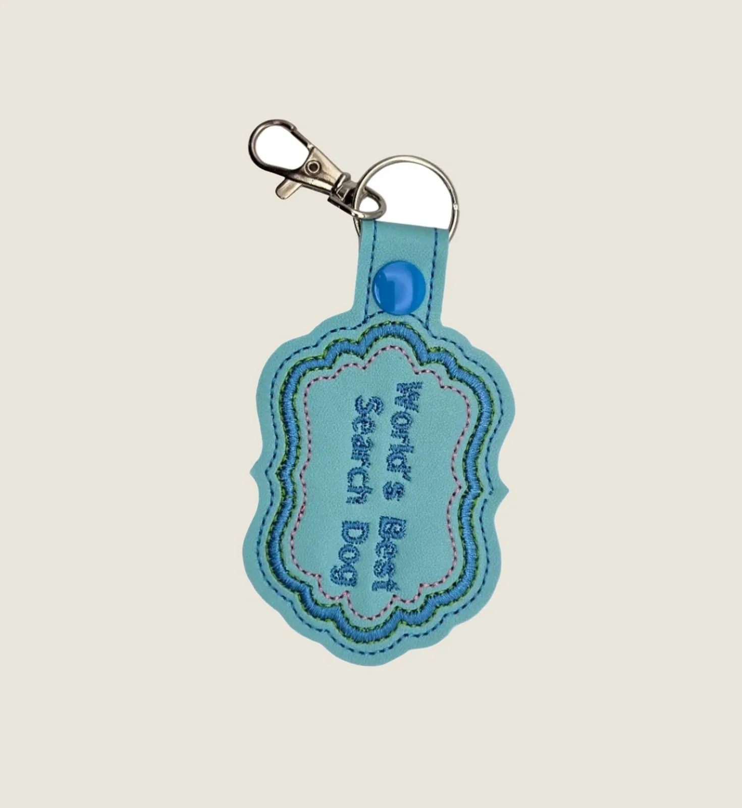 Custom blue faux-leather keychain featuring "World's Best Search Dog" in high-density embroidery, ideal for dog sport gear.