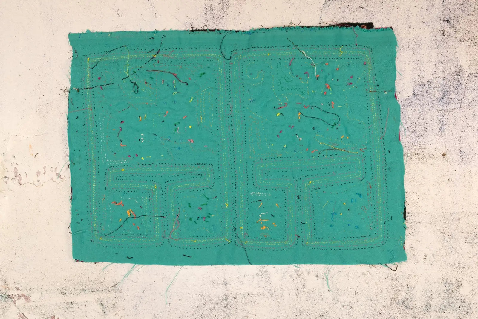 Hand-stitched turquoise textile featuring colorful threads, showcasing intricate design inspired by indigenous culture.