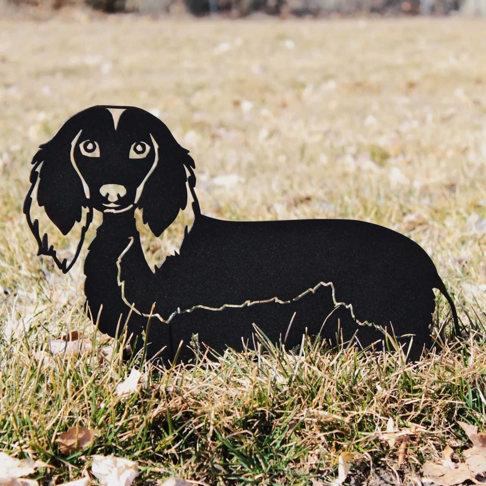 Handmade black metal silhouette of a longhaired Dachshund resting on grass, showcasing its charming design.