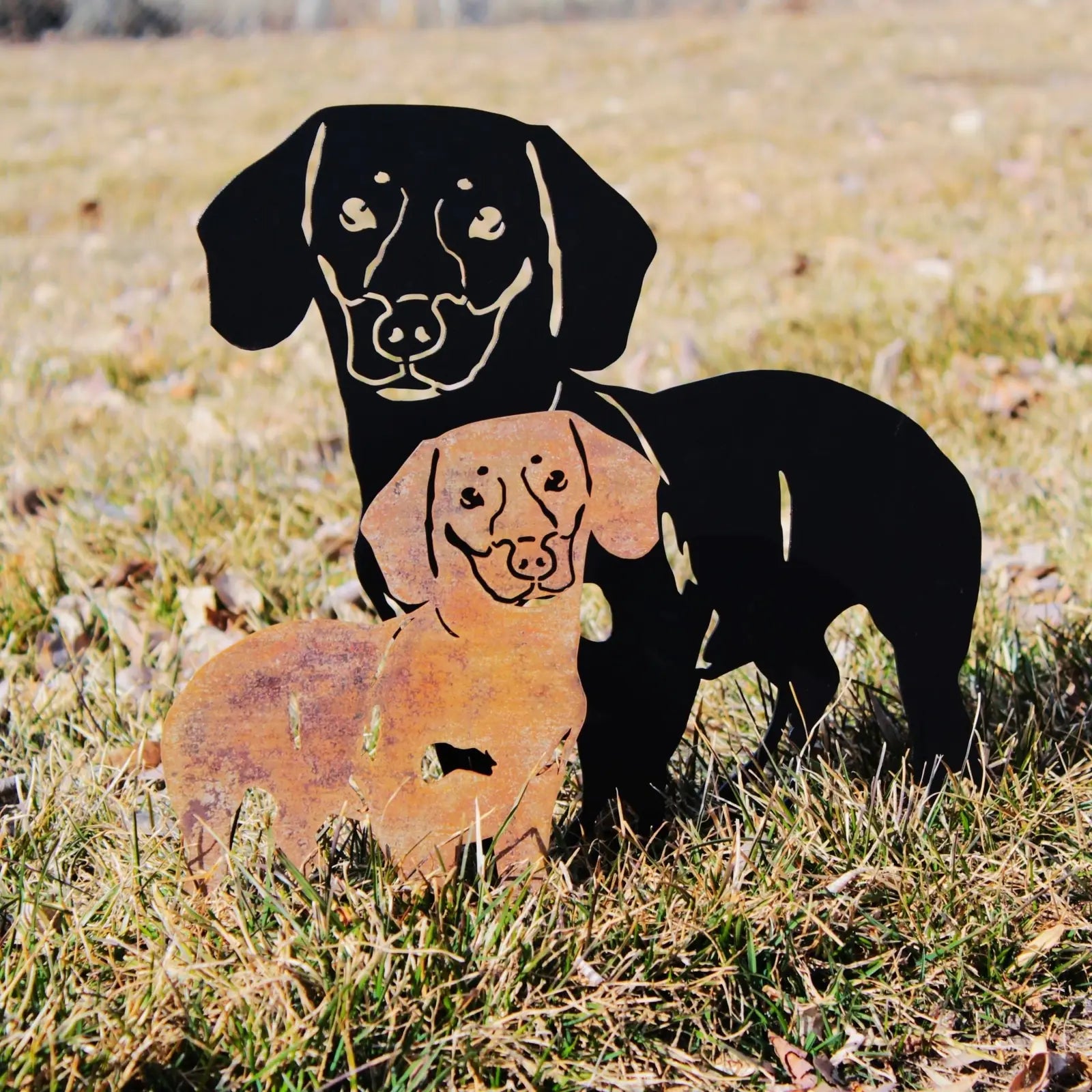 Handmade metal silhouette of two Dachshunds, one black and one rust-colored, displayed on grass for outdoor decor.