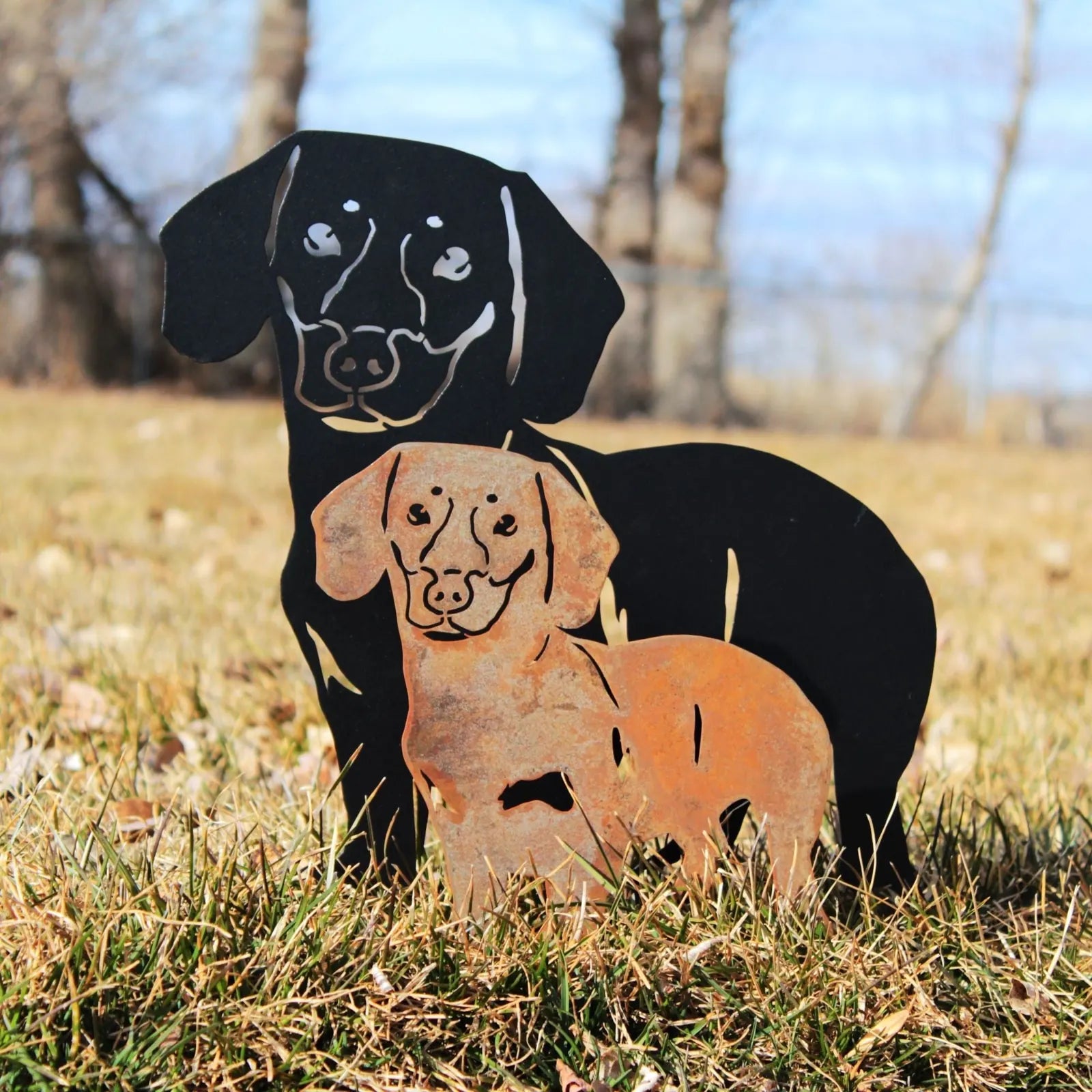 Black and rusty metal silhouettes of a Dachshund and a Labrador in a grassy outdoor setting, showcasing dog breed art.