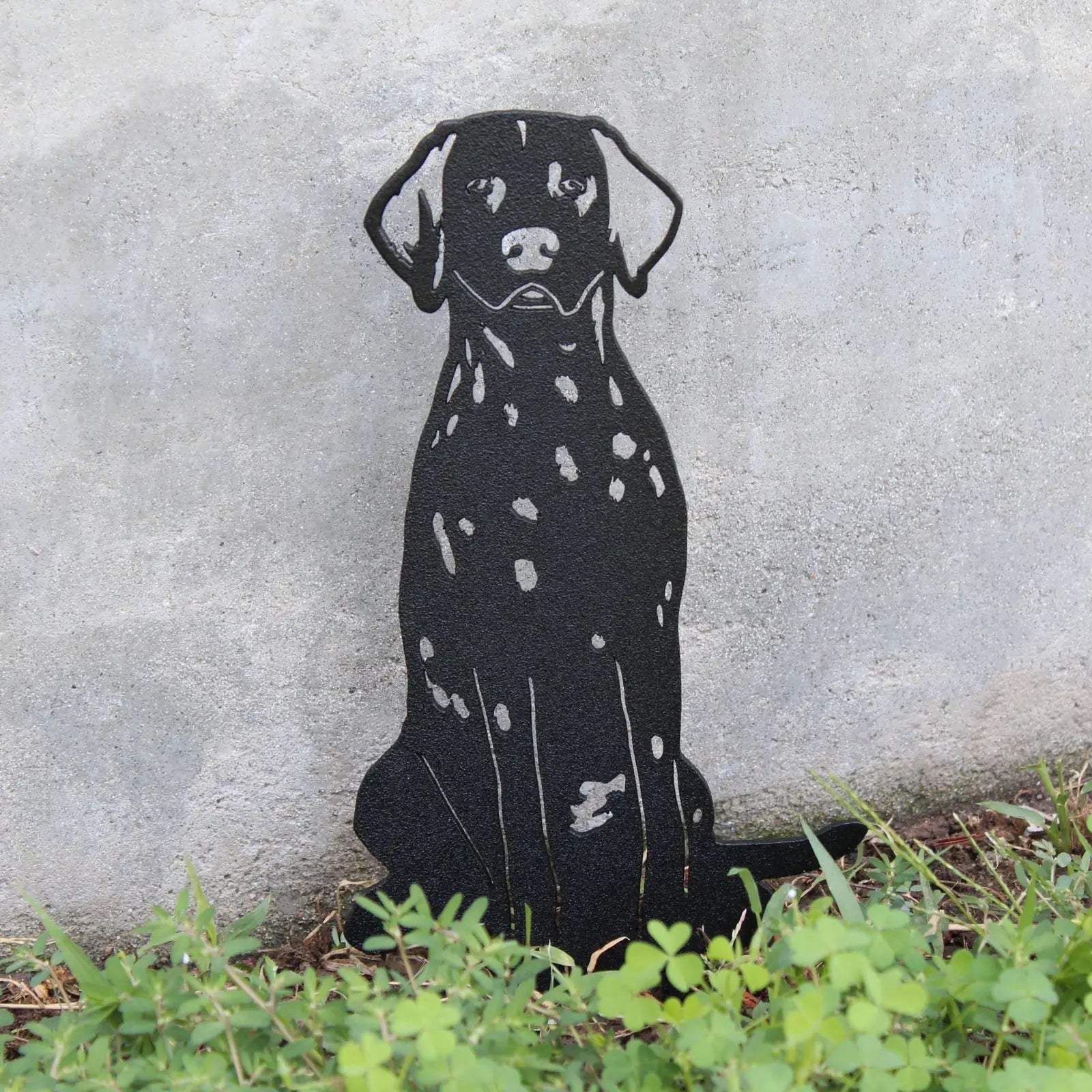 Black Dalmatian metal silhouette art installed in greenery against a textured concrete wall, showcasing its outdoor decor...