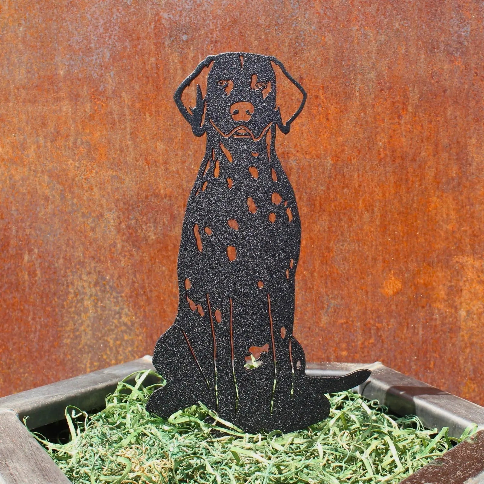 Dalmatian metal silhouette in matte black, perched on green shredded grass in a decorative planter.