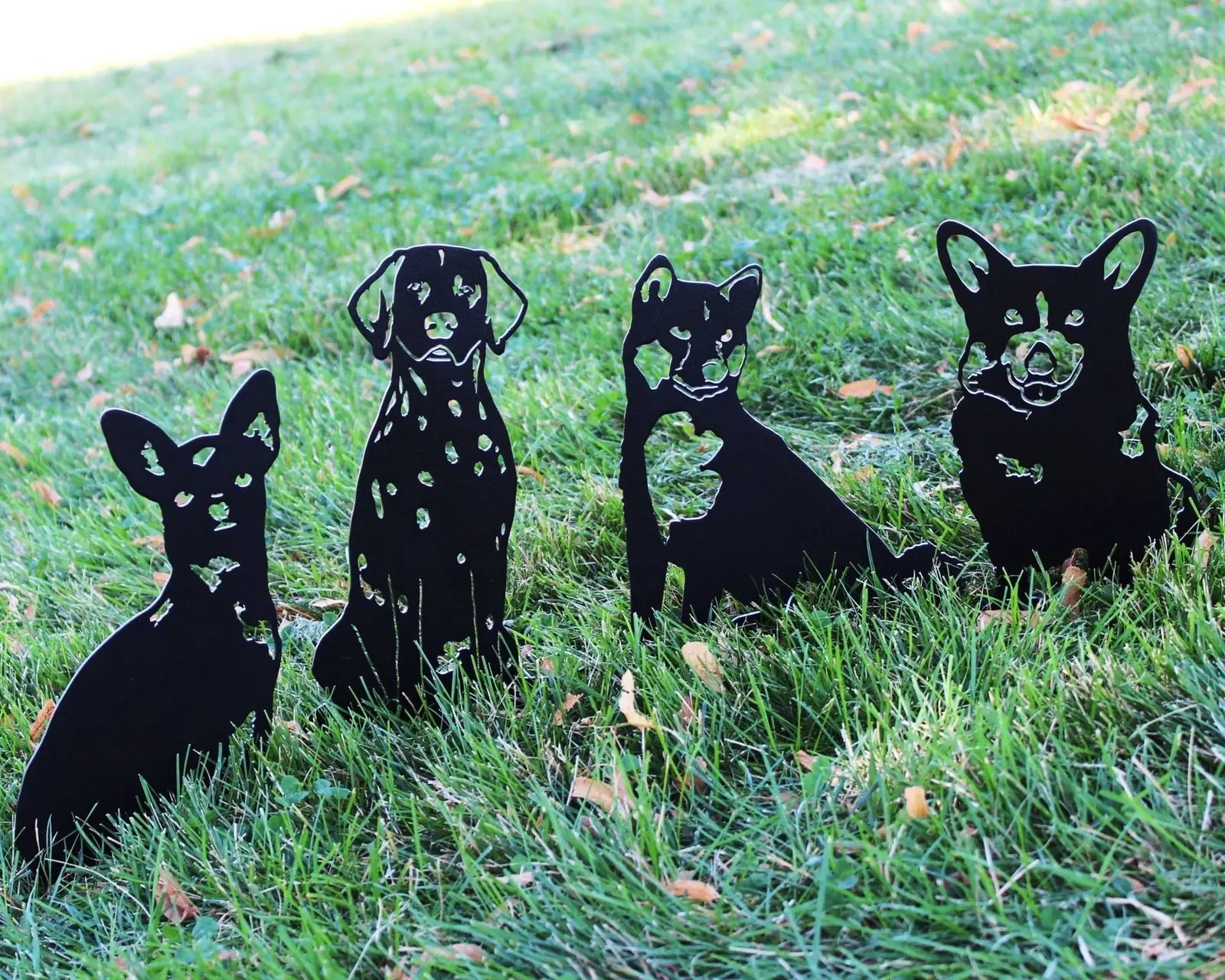 Black metal dog silhouettes of various breeds stand on green grass, showcasing outdoor decor for gardens and yards.