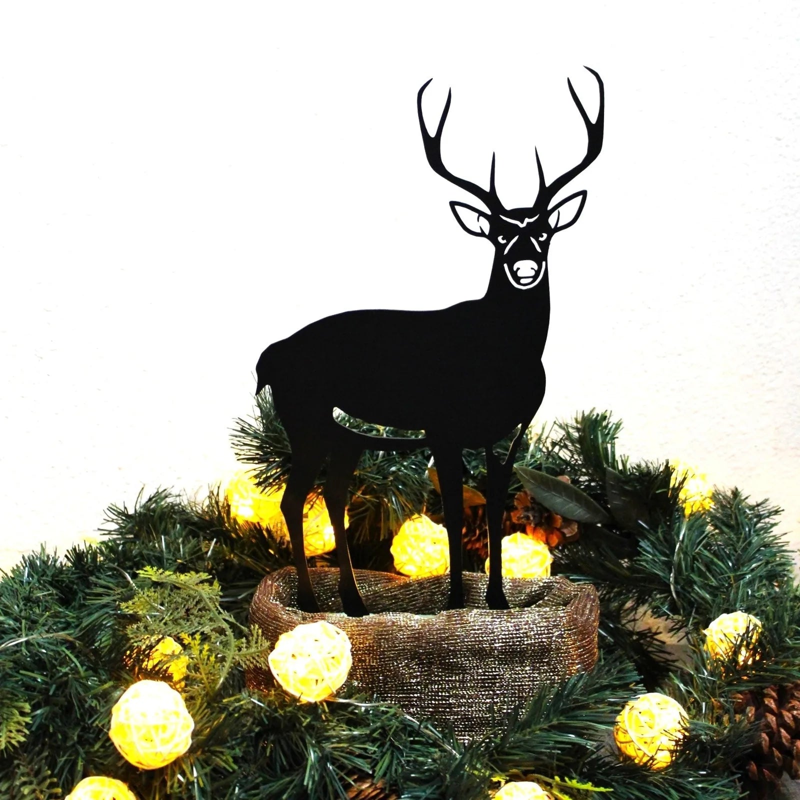 Black metal deer silhouette set among holiday greenery and yellow decorative lights. Ideal for outdoor decor.