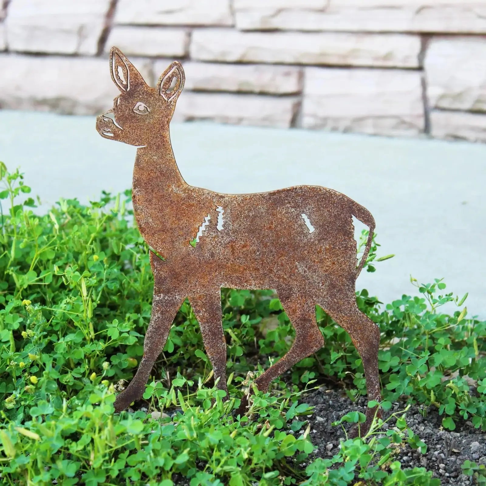 Rusty Corten steel deer silhouette standing among vibrant greenery, showcasing intricate design and weathering details.