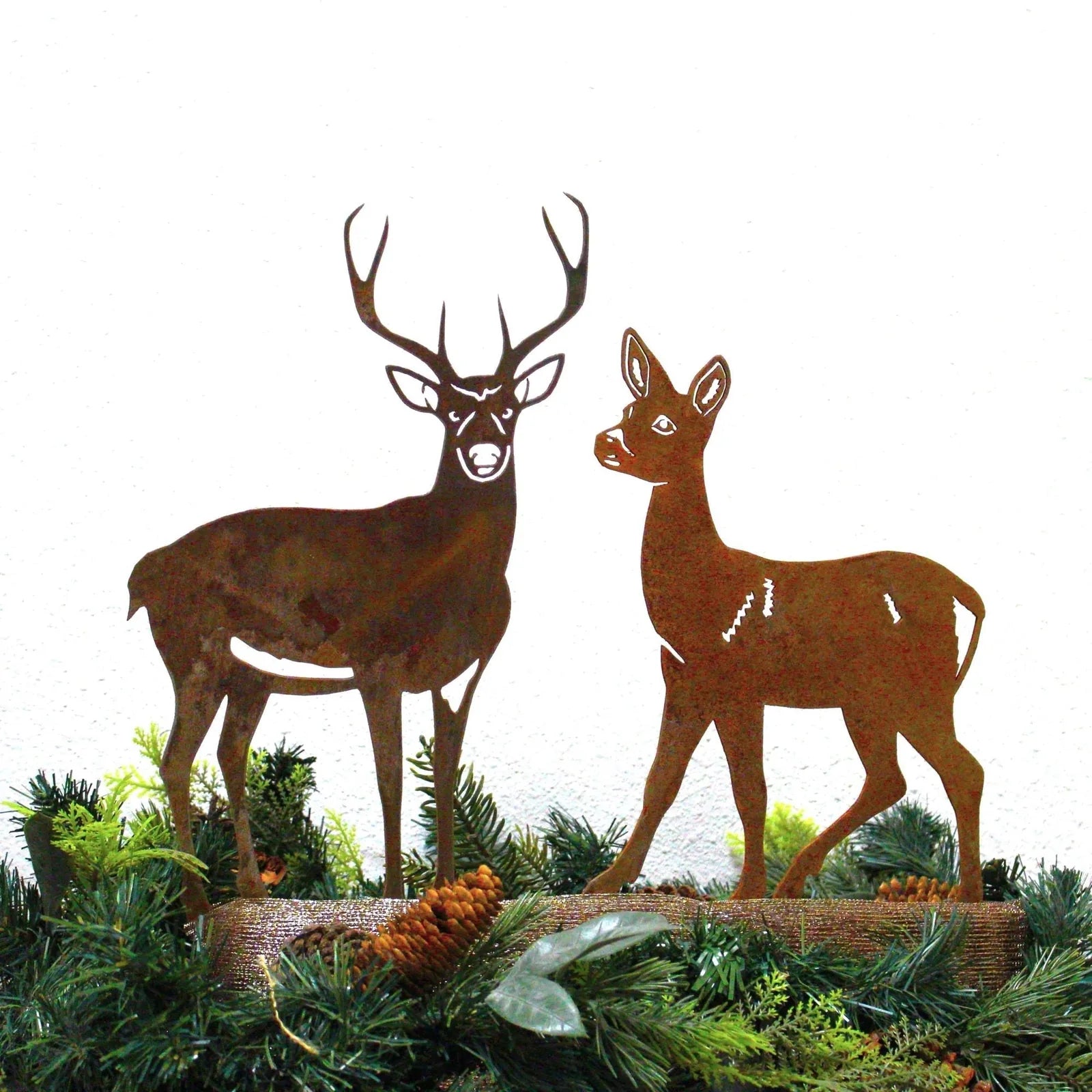 Corten steel deer and doe silhouettes with a rustic patina, framed by greenery and pinecones.