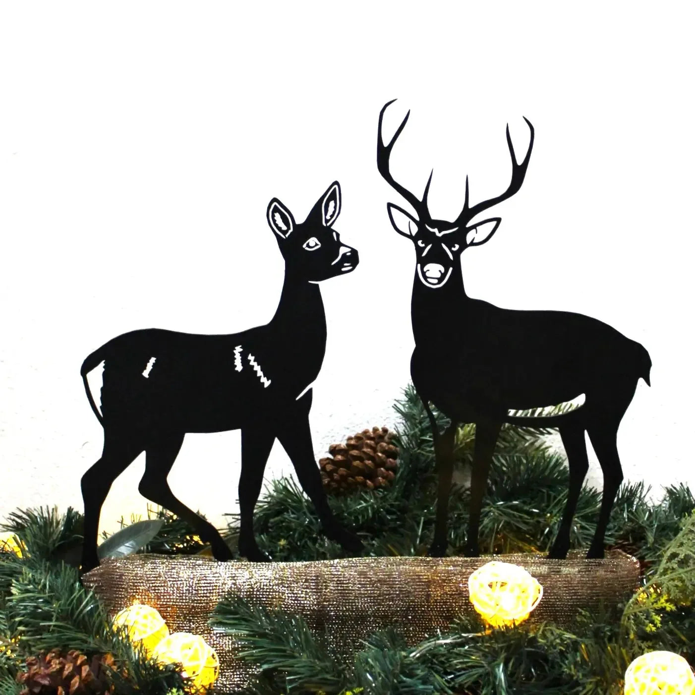 Black metal deer silhouette art featuring a doe and a buck, surrounded by festive greenery and lights.