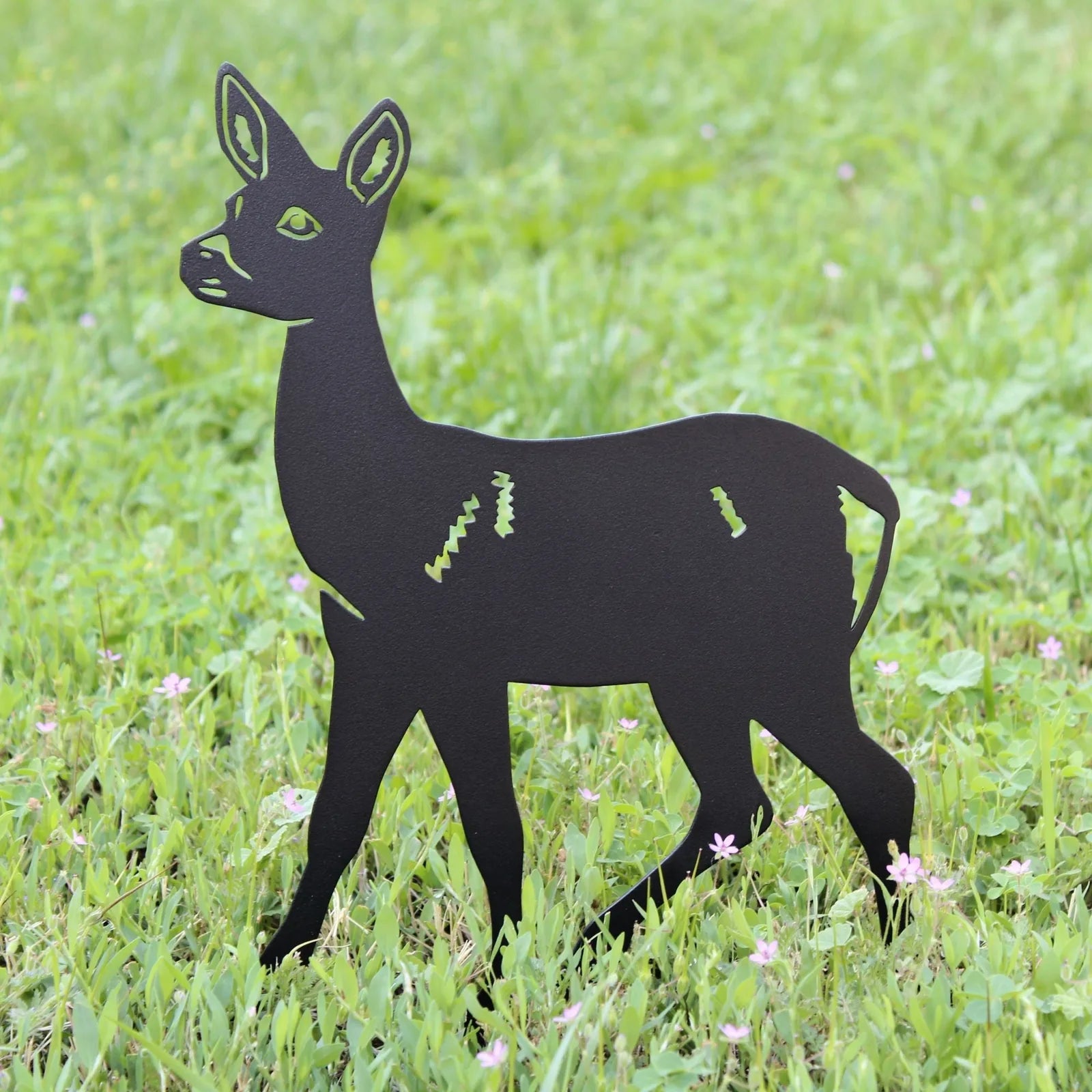 Black metal deer silhouette resting on green grass, showcasing detailed cutouts and an elegant design.