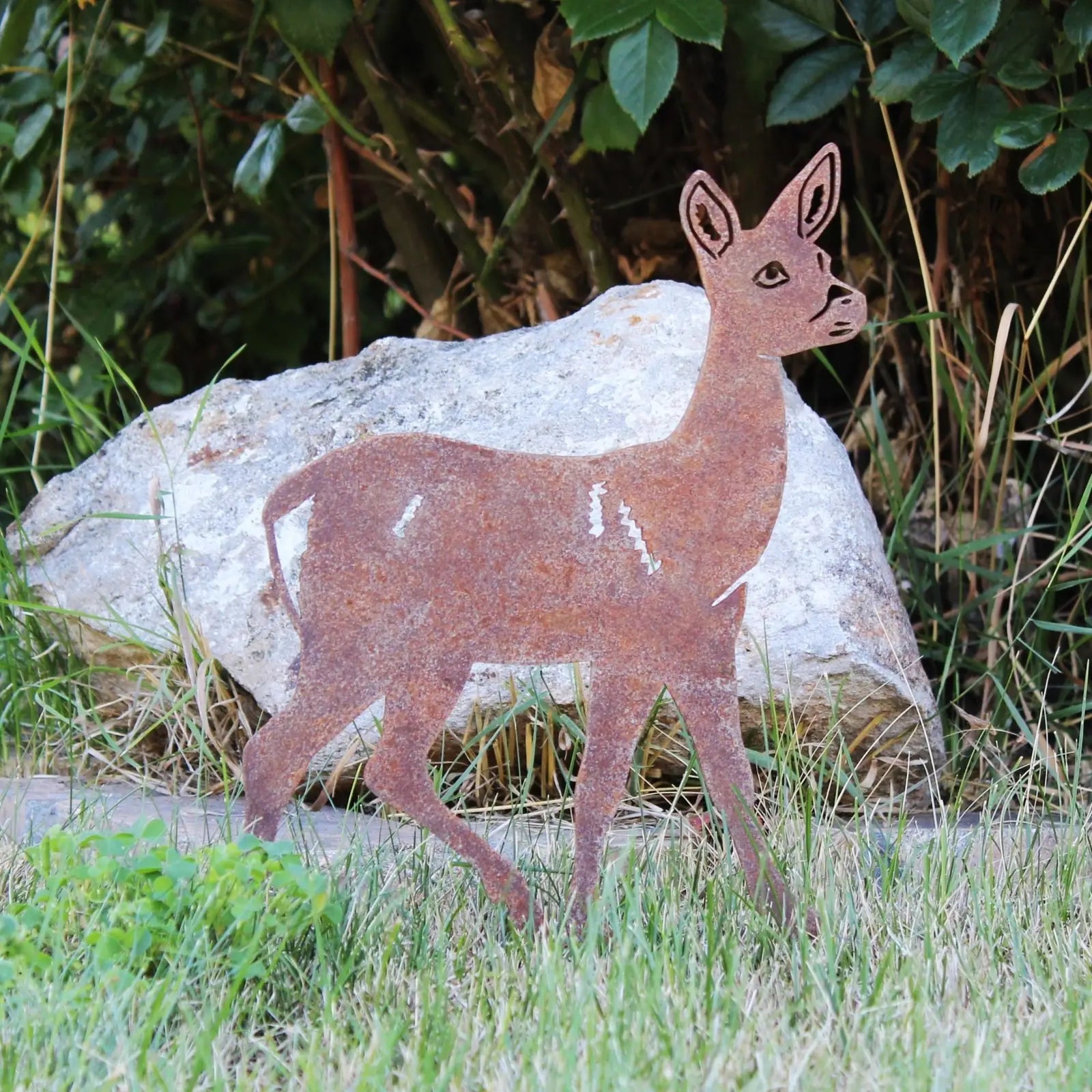 Corten steel deer silhouette in weathered rust finish, set against grass and rocks, showcasing its handmade design.