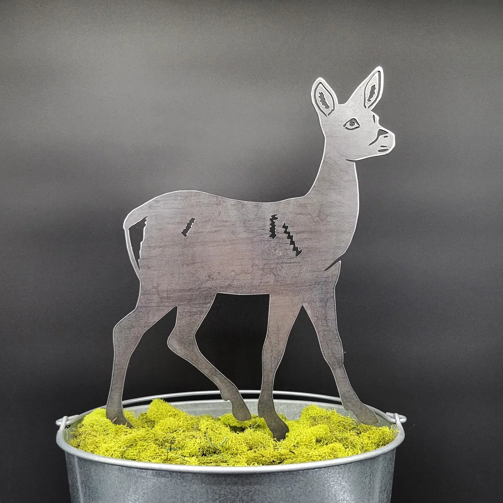 Handmade deer silhouette in Corten steel, mounted on bright green moss in a metal bucket.