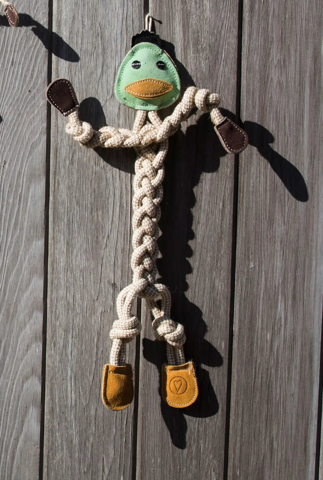 Dilly Duck rope dog toy in natural cotton and hemp, featuring a green head and brown leather accents, hangs on wooden surf...