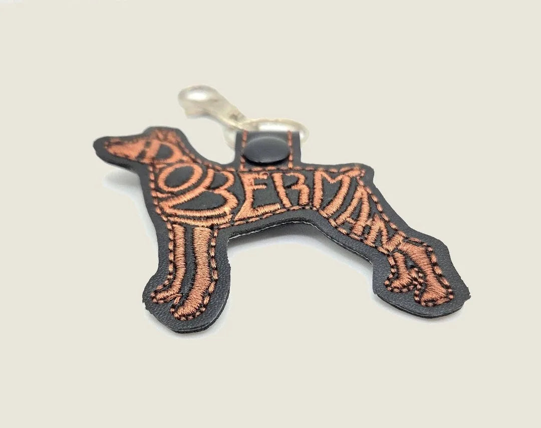 Embroidered Doberman silhouette keychain in black faux leather with copper stitching, ideal for dog lovers.