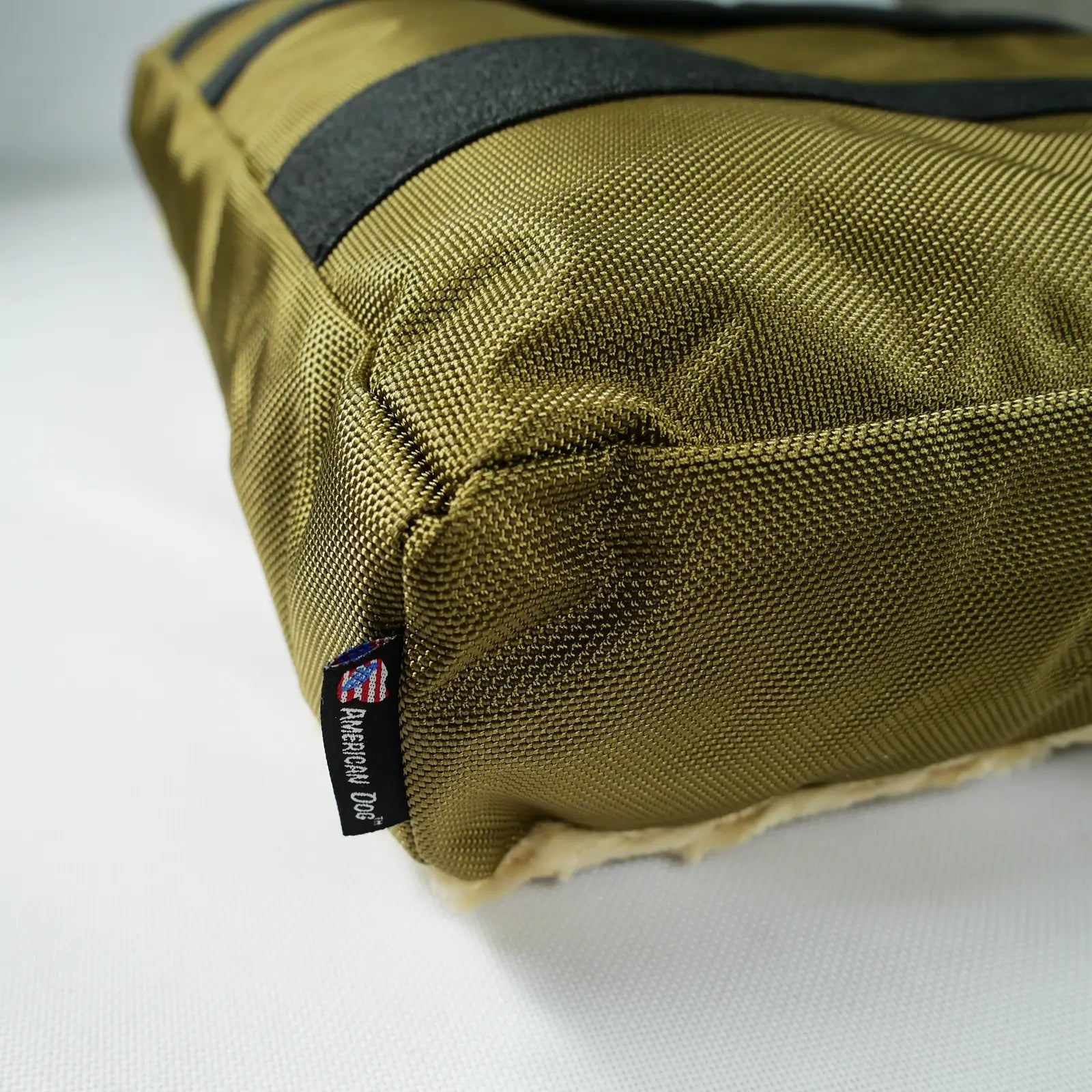 Olive dog bed corner featuring durable nylon fabric, non-skid bottom, and American Dog tag for identification.
